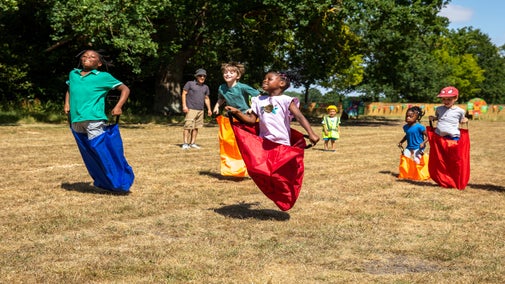 5 children of mixed ages enjoy a sack race on the Wimpole Estate Summer of Play field